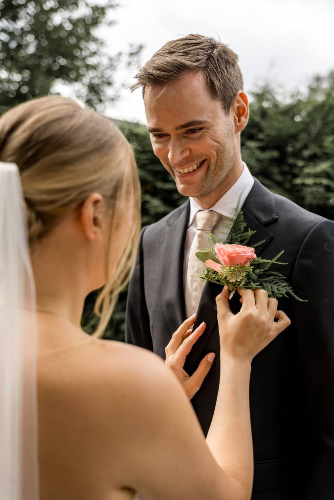 brud justerer knapphullsblomst på brudgommens dress