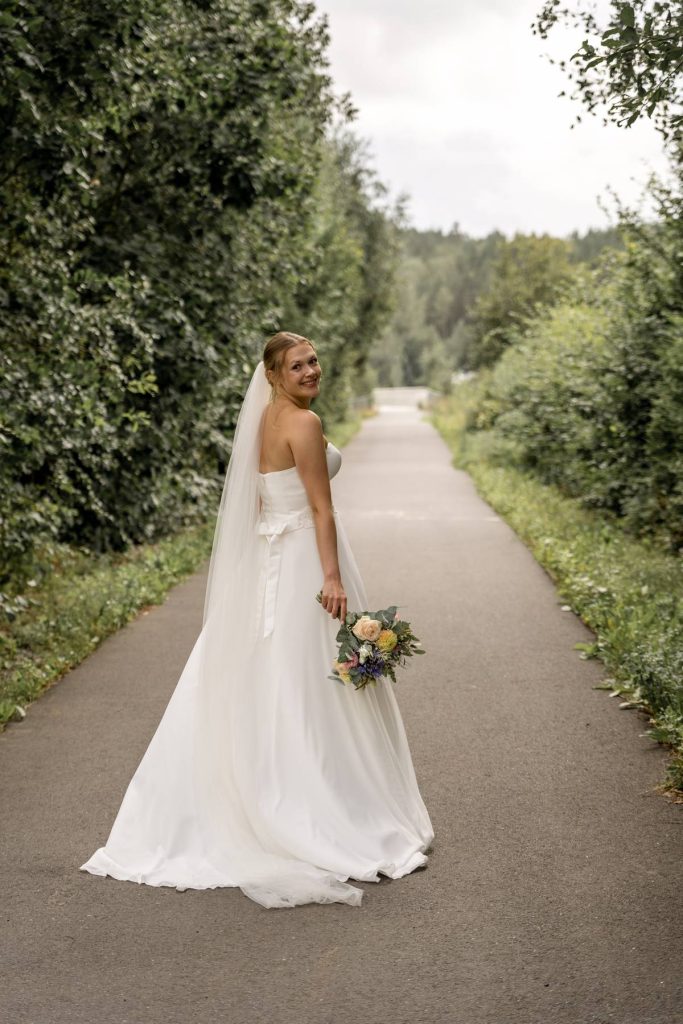 brud går på sti i naturen i vestby og ser tilbake med buketten i hånden