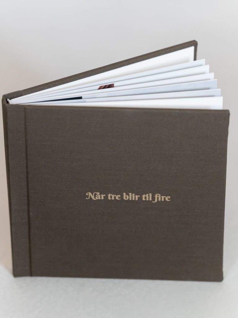 Mørkt fotoalbum med tekst på forsiden og tykke sider med fotografier innvendig